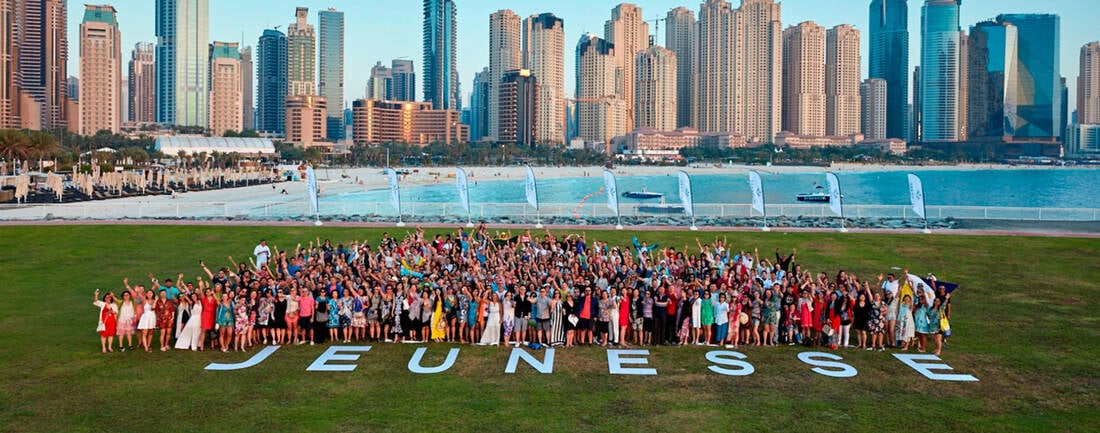 The word JEUNESSE laid out on the ground on a green lawn and the team posing behind it for a picture