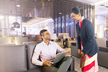 A man and woman sat in an airport lounge with food and drink on their table
