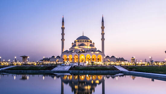 The Sharjah Grand Mosque from across a lake, illuminated by lights at dusk
