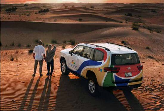 A couple standing in the desert next to an Arabian Adventure Car at sunset