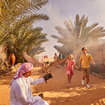 Kids at a desert camp in Dubai running towards a man dressed up in an Emirati outfit holding up an eagle