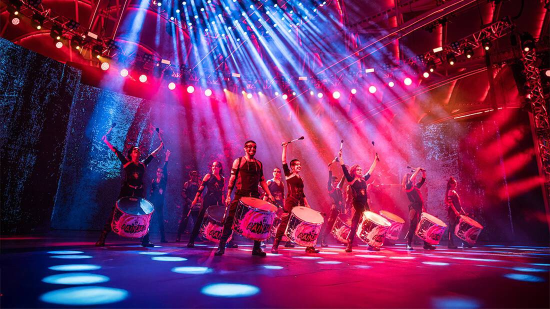 A group of drummers performing at night on the Global Village stage
