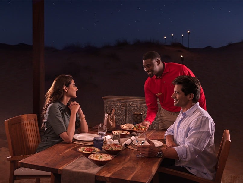 A couple being served food by an Arabian Adventures representative in the desert
