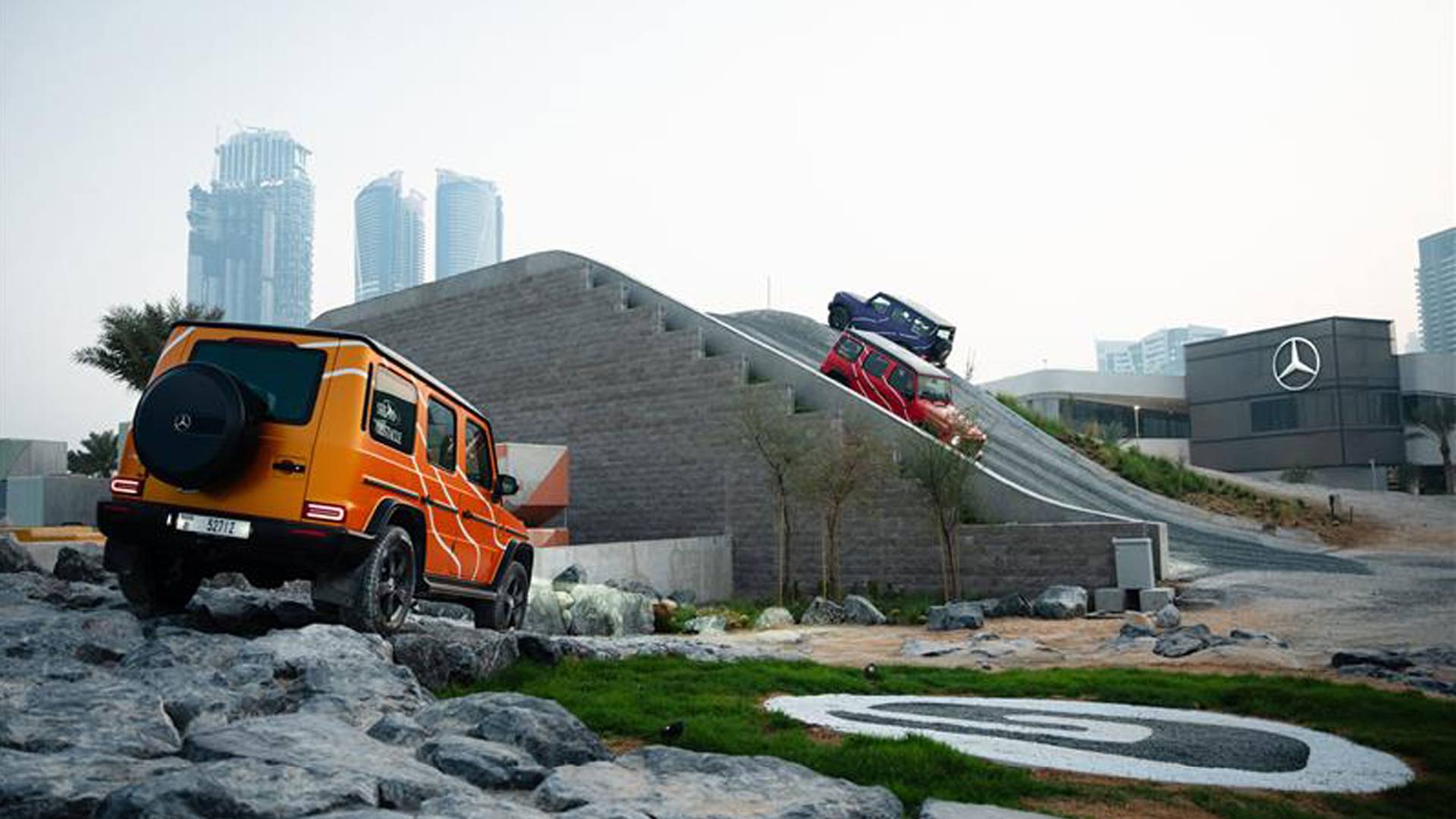 Three colorful Mercedes Benz G Class cars moving around an off-roading city course
