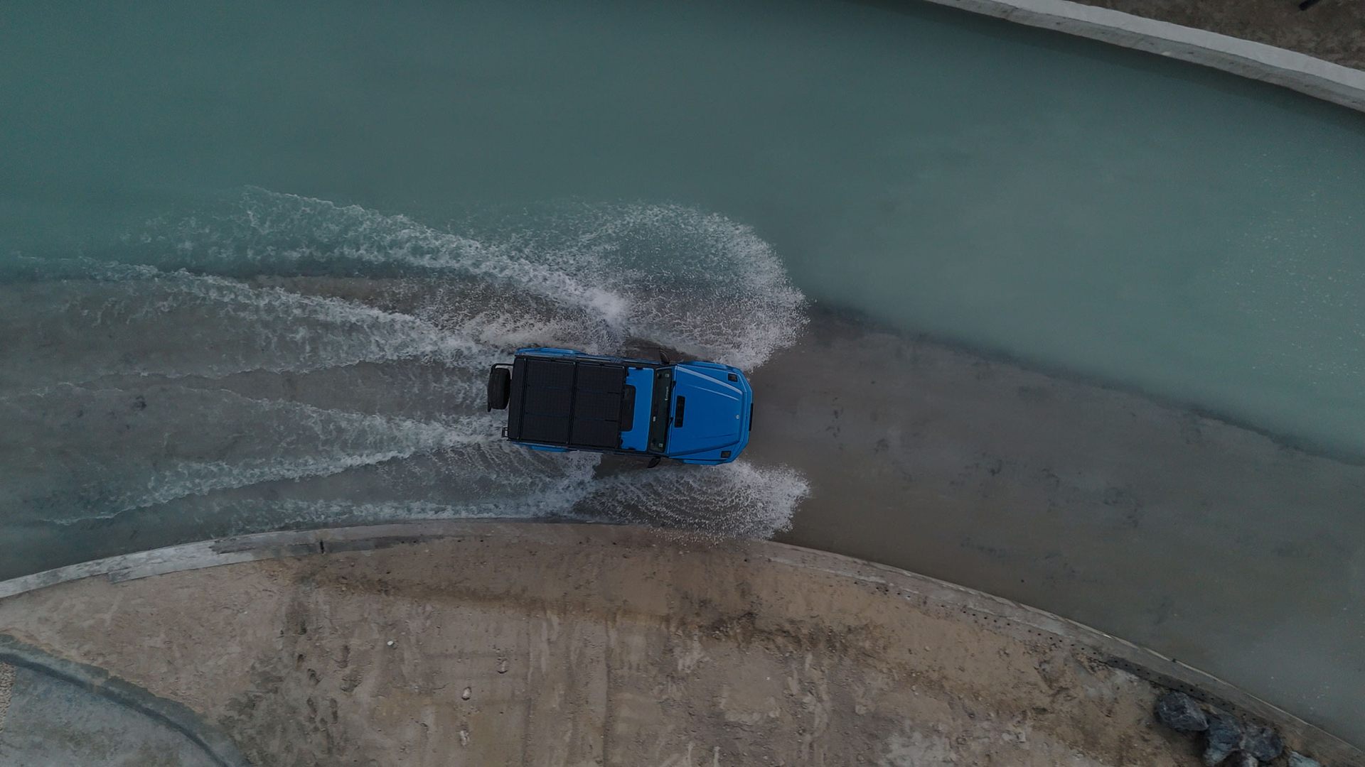 A blue Mercedes Benz driving through a watery road