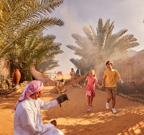 Two kids running towards a man holding up a falcon at the entrance of a desert camp
