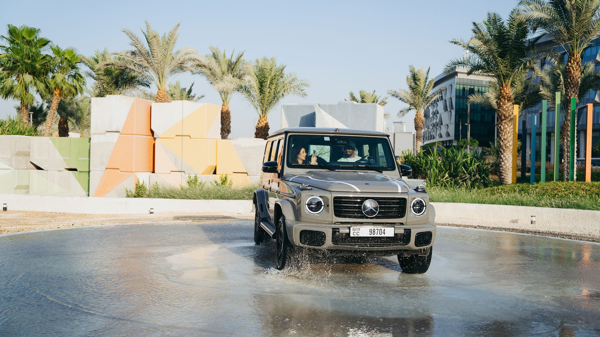 A lady and man inside a grey G-Class driving through a water puddle