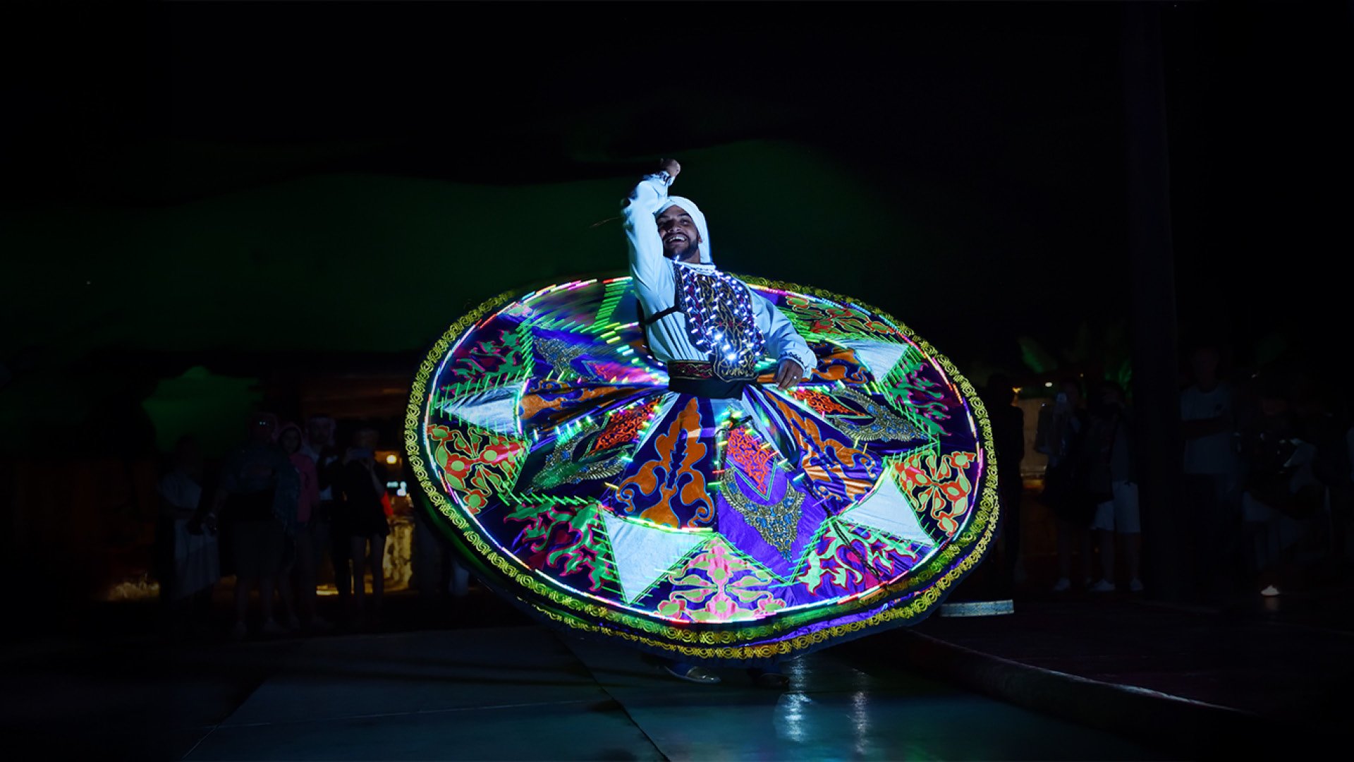 A man performing with a lit up tanora at night