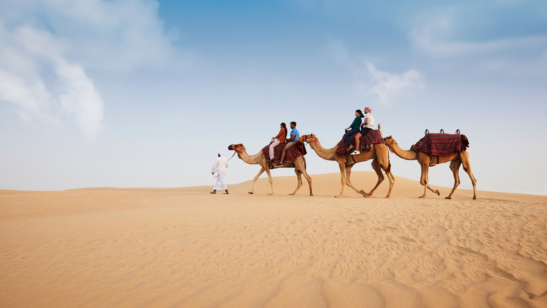 A family on a camel ride in the desert lead by a guide